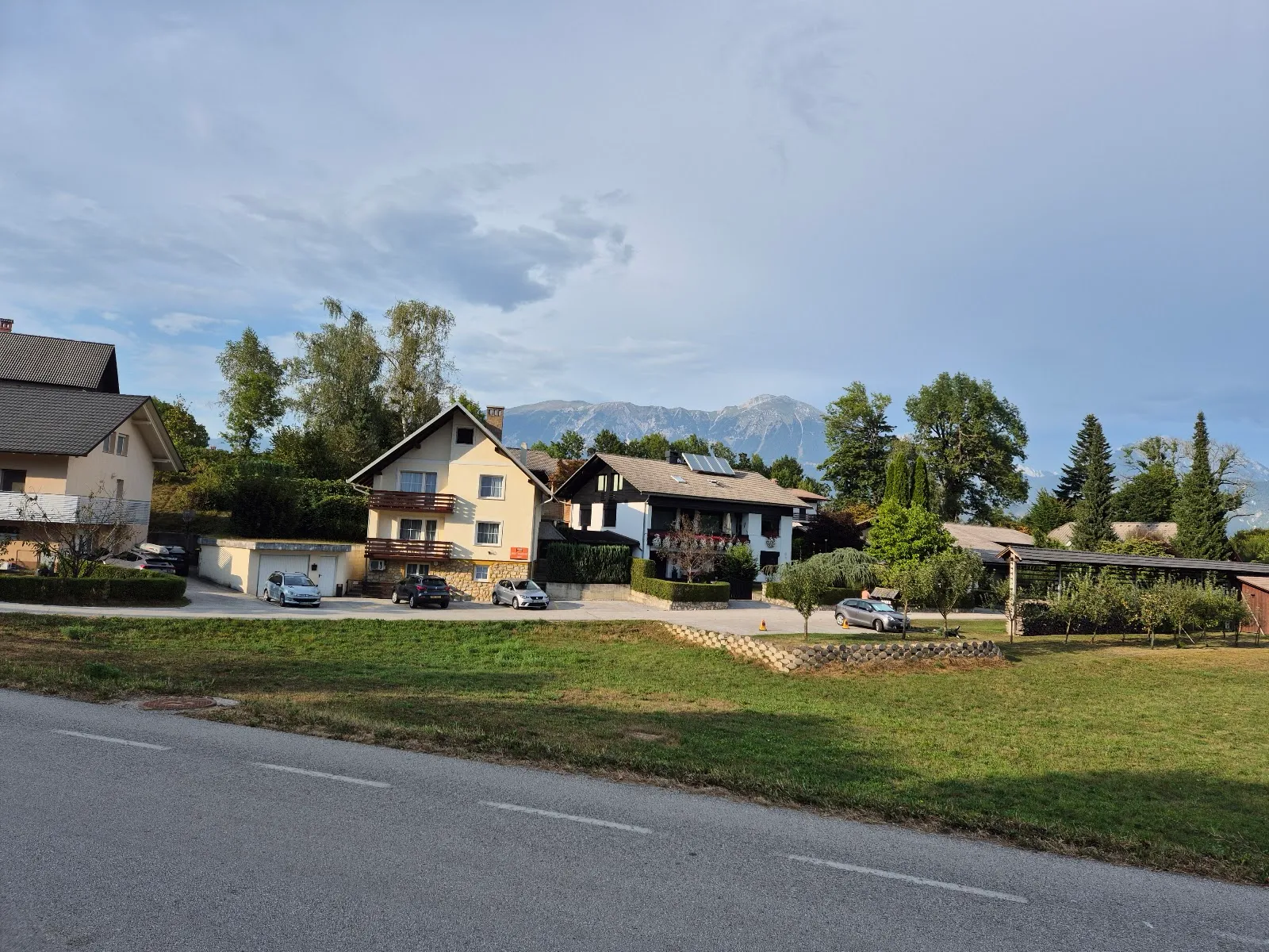 Travnik ob cesti, hiše in gore v ozadju
